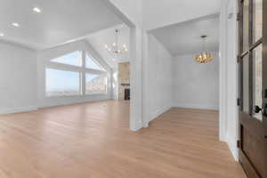 Entrance foyer featuring office chandelier, high vaulted ceiling, light wood-style floors, stone fireplace, and recessed lighting