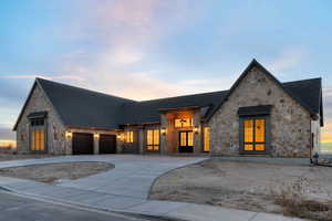 View of front of home featuring copper rain gutters, stone siding, driveway, and roof with shingles