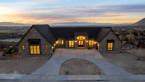 Aerial view of front facade featuring copper rain gutters, stone siding, driveway, and roof with shingles