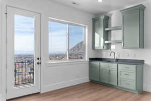 Wet-bar featuring green cabinetry, dark countertops, light wood finished floors, valley and mountain views, and entrance to back deck