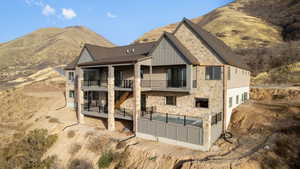 Rear view of house with pool, spa, copper rain gutters, stone siding, mountain view, and decks with sitting areas