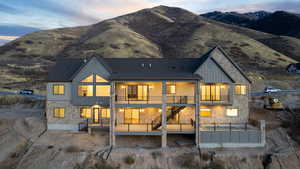 Back of house at dusk featuring pool, spa, copper rain gutters, stone siding, board and batten siding, decks with valley and mountain views, and stairway between decks