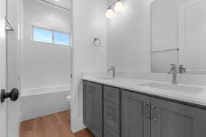 Full bath featuring double vanity and light wood-style flooring, between basement bedrooms