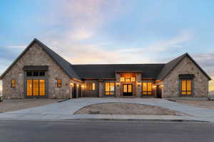 View of front facade featuring copper rain gutters, stone siding, concrete driveway, and roof with shingles