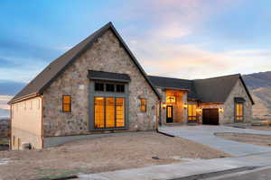 View of front of house with copper rain gutters, concrete driveway, stone siding, roof with shingles