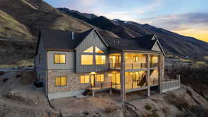 Back of property at dusk with pool, spa, copper rain gutters, stone siding, board and batten siding, decks with valley and mountain views, and stairway between decks