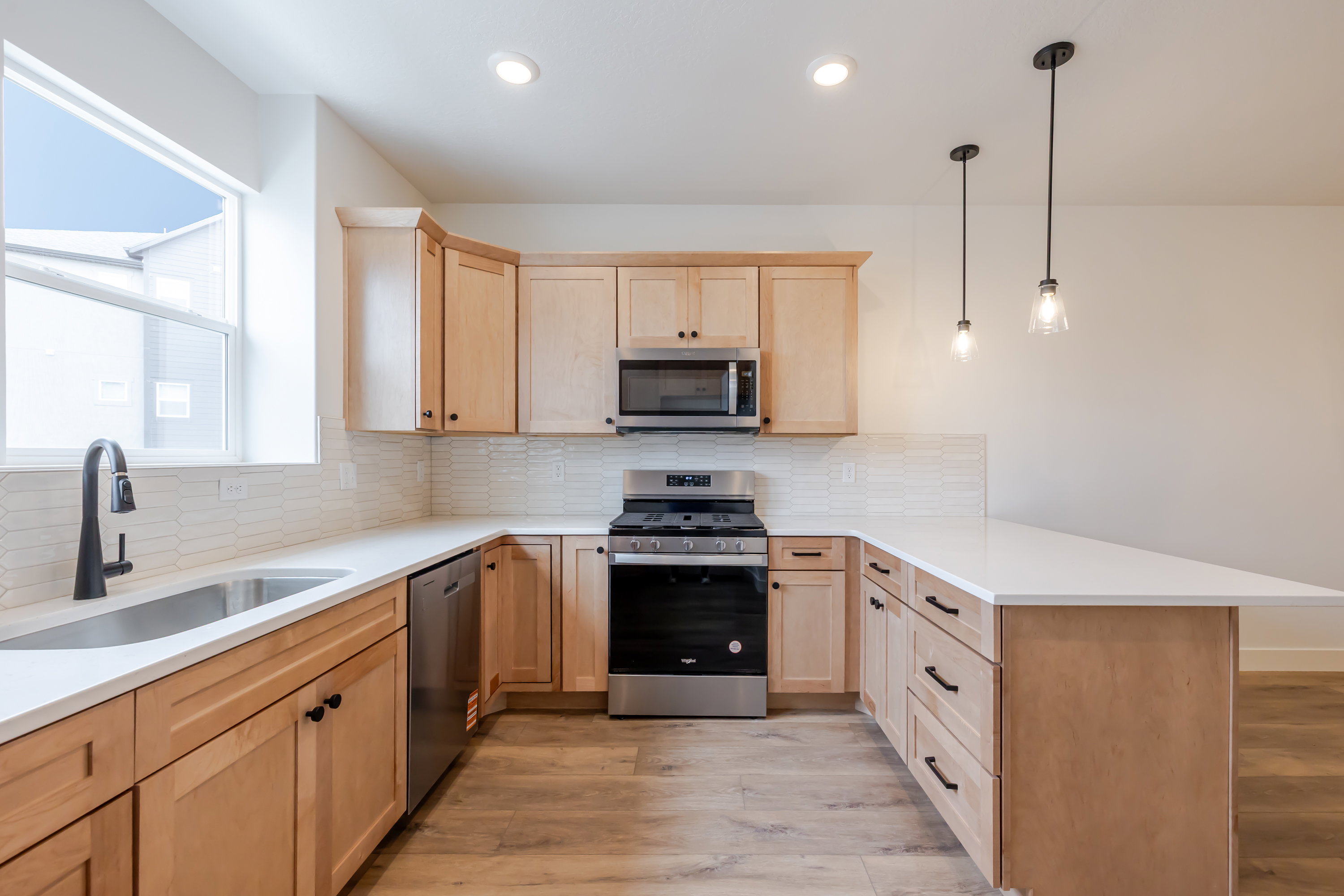 Kitchen featuring stainless steel appliances, light wood finish cabinetry, light wood finished floors, a peninsula, and tasteful backsplash