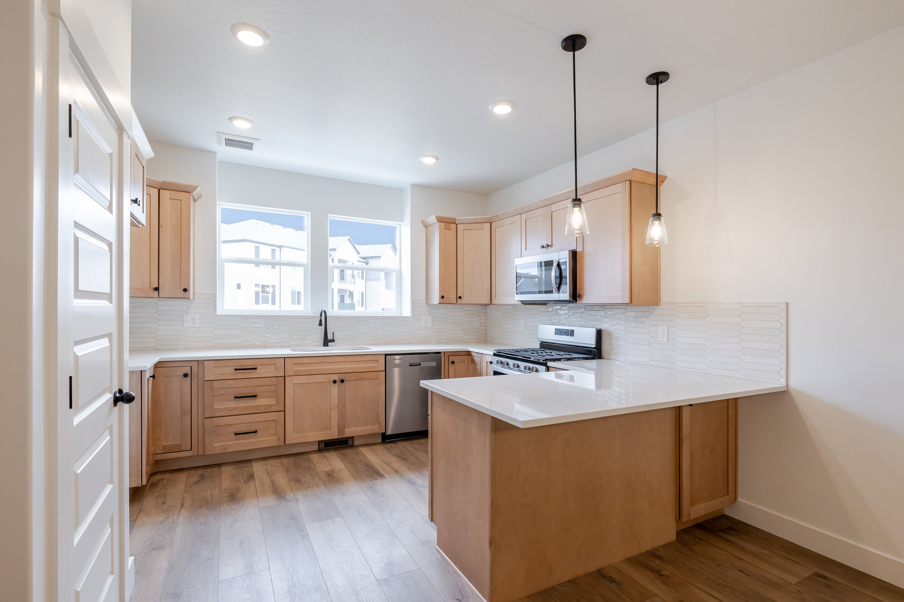 Kitchen with a peninsula, light wood finish cabinetry, decorative backsplash, and stainless steel appliances