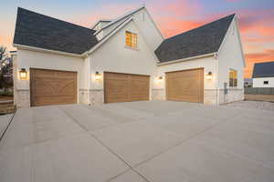 View of front facade with stone siding, driveway, a shingled roof, and stucco siding
