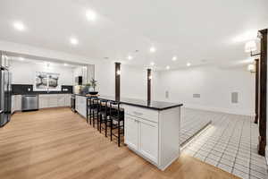 Kitchen with light wood-type flooring, stainless steel appliances, white cabinetry, a peninsula, and open floor plan