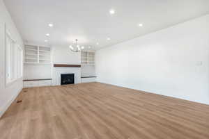 Unfurnished living room featuring light wood-type flooring, a fireplace, recessed lighting, built in features, and a chandelier