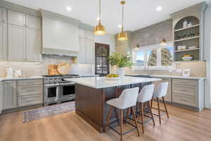 Kitchen with range with two ovens, a breakfast bar area, decorative light fixtures, light stone counters, and a kitchen island
