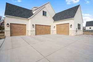 View of front of property with stone siding, stucco siding, concrete driveway, and a shingled roof