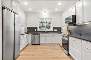 Kitchen with stainless steel appliances, white cabinetry, light wood finished floors, recessed lighting, and dark stone counters