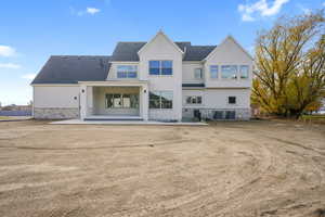 Back of property with a patio area, stone siding, stucco siding, and a shingled roof