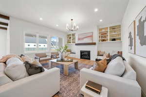 Living area with suspended lighting, a brick fireplace, built in shelves, and wood finished floors