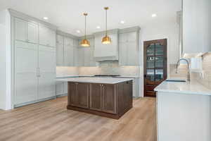 Kitchen with a kitchen island, light stone counters, light wood-style floors, hanging light fixtures, and recessed lighting