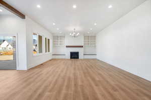 Unfurnished living room featuring recessed lighting, light wood-style flooring, a fireplace, a chandelier, and built in shelves