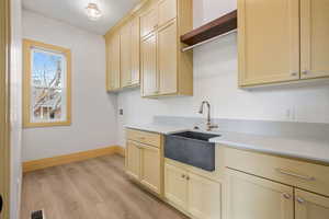 Kitchen with light wood-style flooring, cream cabinetry, open shelves, and light stone countertops