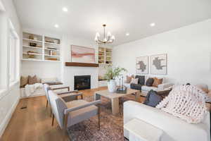 Living room featuring wood finished floors, hanging lights, a brick fireplace, and built in shelves