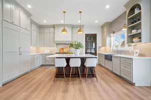 Dual tone kitchen featuring hanging light fixtures, a kitchen breakfast bar, a center island, light wood-style floors, and light stone countertops