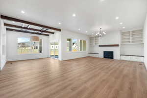 Unfurnished living room featuring recessed lighting, plenty of natural light, a fireplace, beam ceiling, and light wood-style flooring