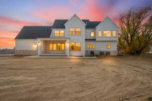 Back of property at dusk with a patio, stucco siding, roof with shingles, and stone siding