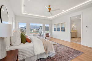 Bedroom with light wood finished floors, a ceiling fan, recessed lighting, ensuite bath, and a raised ceiling