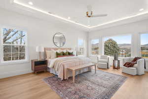 Bedroom with light wood-style floors, a ceiling fan, recessed lighting, a raised ceiling, and a mountain view