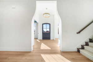 Foyer featuring arched walkways, light wood-style floors, a high ceiling, and stairway