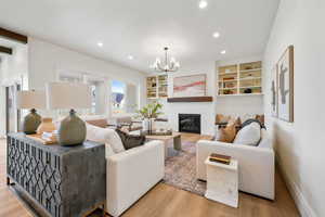 Living room with hanging lights, light wood-type flooring, a fireplace, a baseboard heating unit, and built in shelves