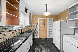 Kitchen featuring open shelves, freestanding refrigerator, white cabinets, tasteful backsplash, and decorative light fixtures