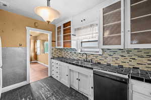 Kitchen featuring white cabinets, black dishwasher, decorative light fixtures, backsplash, and tile counters