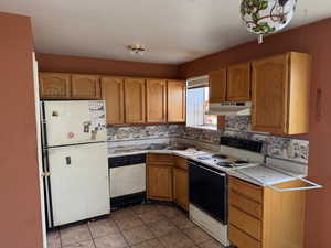 Kitchen featuring white appliances, brown cabinets, light countertops, under cabinet range hood, and light tile patterned flooring