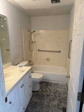 Full bathroom featuring vanity, shower / bath combination, and dark stone finish floors