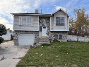 Bi-level home featuring stone siding, an attached garage, concrete driveway, and a chimney