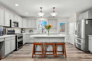 Kitchen with stainless steel appliances, decorative light fixtures, light wood-style floors, backsplash, and recessed lighting