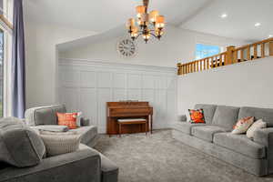 Living area with a chandelier, a decorative wall, carpet, and high vaulted ceiling