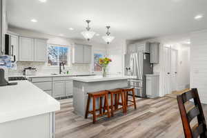 Kitchen with gray cabinets, a kitchen bar, a center island, stainless steel fridge with ice dispenser, and hanging light fixtures