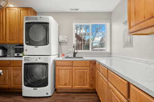 Washroom featuring dark wood-style flooring, stacked washing machine and dryer, and electric panel