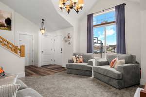 Living room with a chandelier, dark carpet, stairs, and high vaulted ceiling