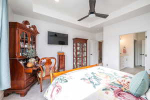 Primary Bedroom featuring light carpet, a tray ceiling, ceiling fan, and ensuite bath