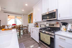 Kitchen featuring appliances with stainless steel finishes, white cabinets, light wood finished floors, backsplash, and recessed lighting
