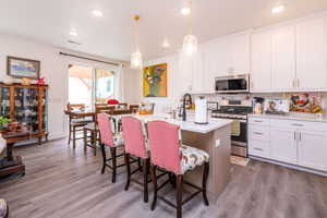Kitchen with white cabinetry, appliances with stainless steel finishes, hanging light fixtures, a breakfast bar area, and an island with sink