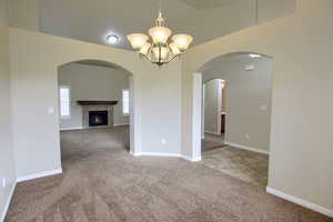 Spare room with light carpet, a chandelier, a fireplace, and arched walkways