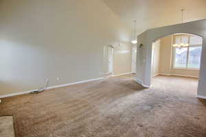 Empty room featuring light carpet, high vaulted ceiling, a chandelier, and arched walkways