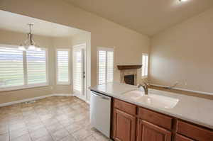 Kitchen featuring brown cabinetry, a chandelier, stainless steel dishwasher, decorative light fixtures, and light tile patterned flooring