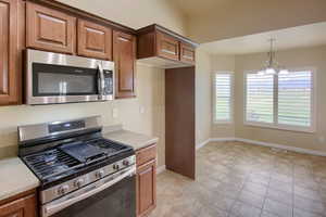 Kitchen with stainless steel appliances, light countertops, a chandelier, hanging light fixtures, and light tile patterned flooring