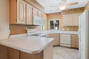 Kitchen featuring light brown cabinetry, white appliances, light countertops, and ceiling fan