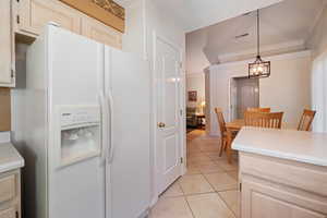 Kitchen with white fridge with ice dispenser, light countertops, light tile patterned floors, light brown cabinetry, and hanging light fixtures